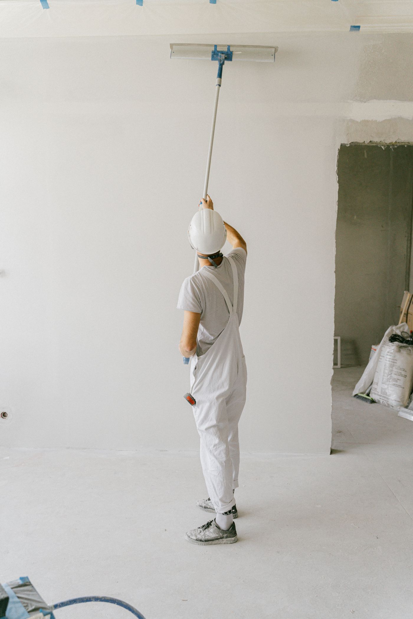 Painter in white overalls and hard hat repainting an interior wall with a roller