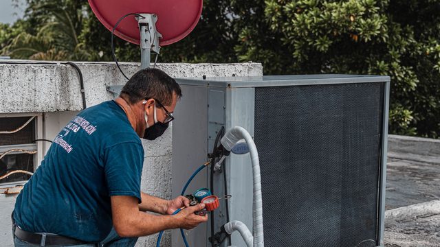 Air-conditioning technician checking a condenser unit with a manifold gauge